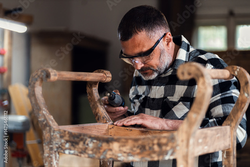 Bilde på lerret Carpenter standing in his workshop restoring old piece of furniture with mini grinder