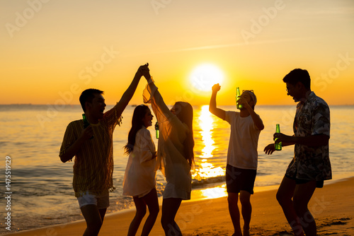 Happy Asian man and woman travel the sea on summer beach holiday vacation. Group of People friends enjoy and fun outdoor lifestyle celebration dancing and drinking beer on tropical beach at sunset.