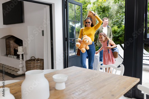 Family arriving home with luggage and teddy bear, smiling and excited