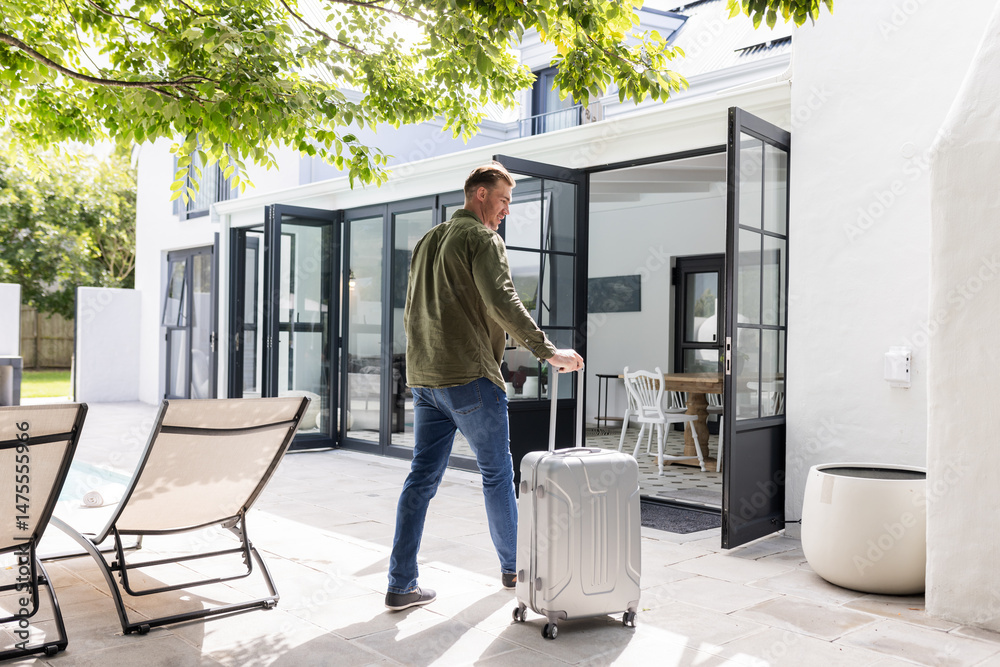 Fototapeta premium Man with suitcase entering modern home through glass doors, ready for travel