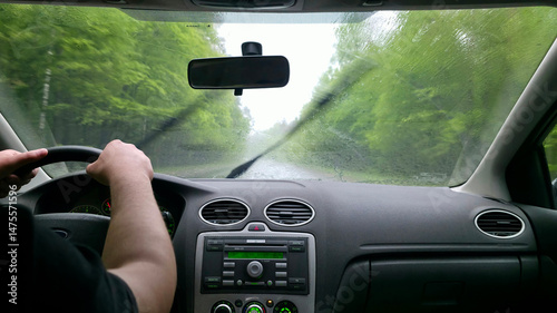 Driving in heavy rain. Interior view from the driver's seat. Wet windshield, blurred road and trees. Focus on the journey. Travel, transportation concept.