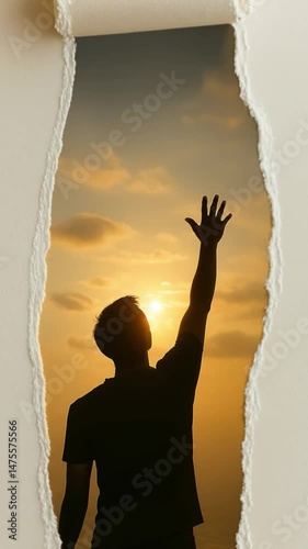 Man reaching towards the sun through a torn wall at sunset in an artistic representation of hope and aspiration
