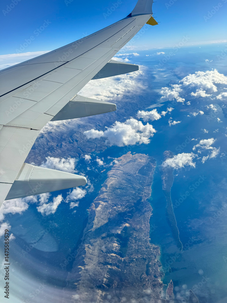 Obraz premium AERIAL: Window seat view on a flight over the dramatic coastline of Croatia. Flying over Adriatic Sea and rolling clouds reveals rugged islands surrounded by blue water. Scenic views during air travel