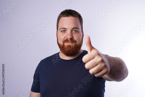 Confident young man showing OK sign. Young guy with ginger beard and blue eyes giving thumbs up.