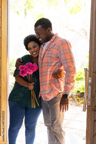 Couple embracing warmly at home, holding vibrant pink flowers, smiling joyfully