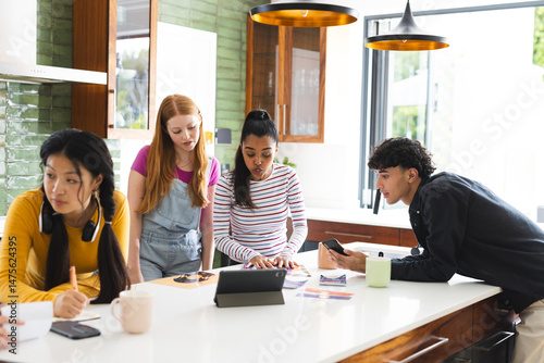Teens collaborating on school project using tablet and smartphones in modern kitchen