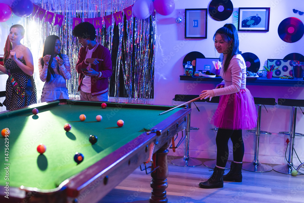 Fototapeta premium Teen playing pool at birthday party, friends enjoying music and snacks nearby