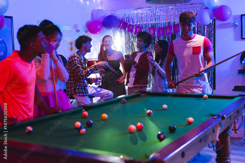 Fototapeta premium Teenagers enjoying lively birthday party playing pool in festive decorated room