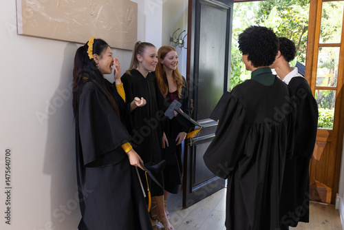 Teens in graduation gowns celebrating together at home, smiling and chatting