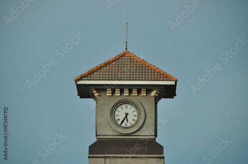 Architectural clock tower with a tiled roof photographed against a clear blue sky.