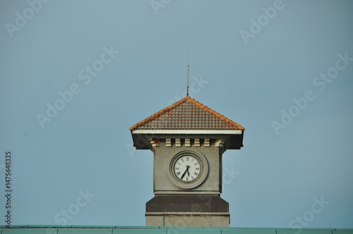 Architectural clock tower with a tiled roof photographed against a clear blue sky.