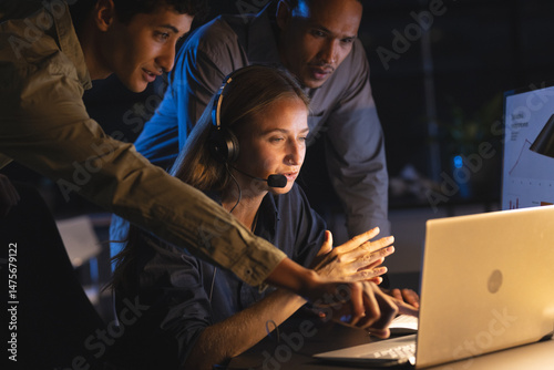 Team collaborating at night, focused on laptop screen, discussing project details