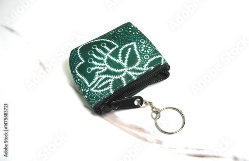 A close-up of a hand-carved keychain made from green stone, decorated with white floral patterns.