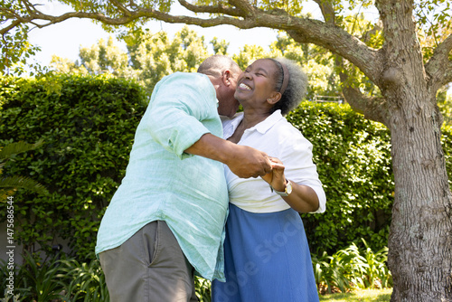 African American senior couple dancing joyfully under tree in sunny garden