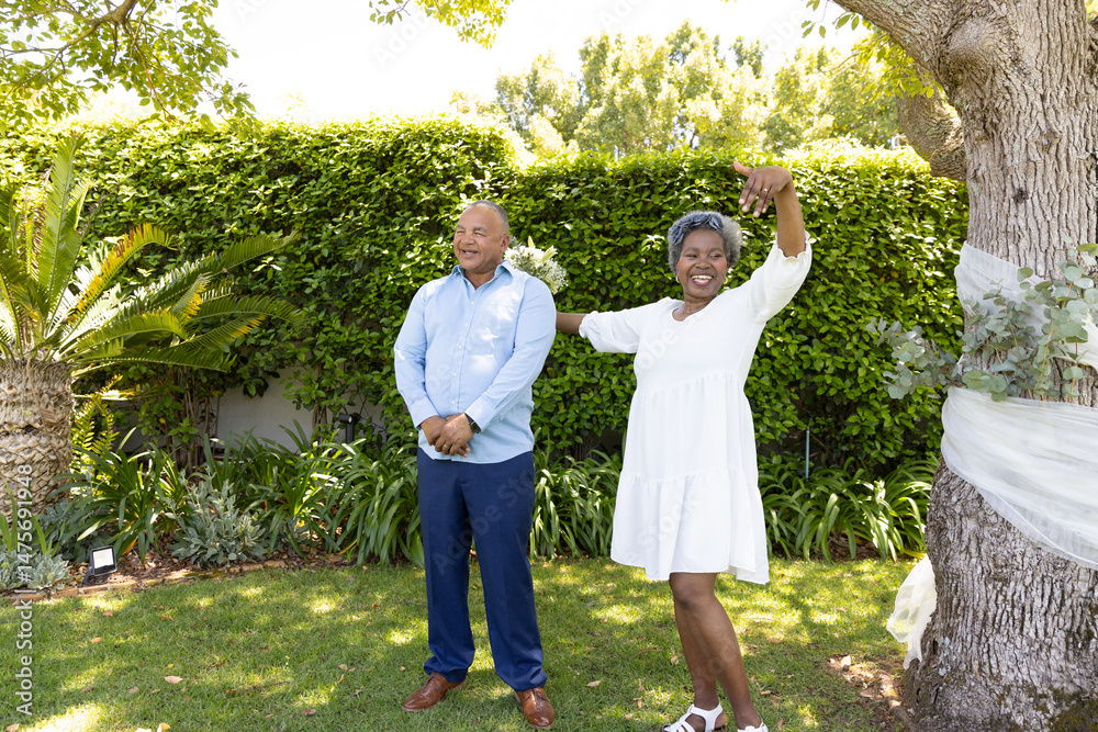 Fototapeta premium Senior couple enjoying sunny day in garden, woman dancing joyfully beside partner