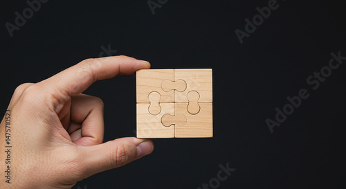 A hand holding a small square puzzle made of four wooden pieces against a dark background in a studio