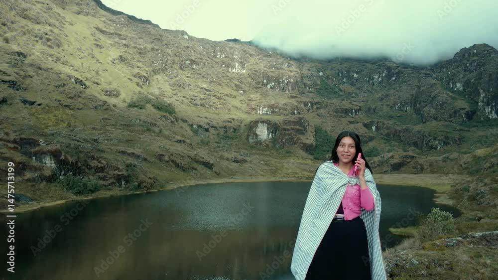 Video de una feliz y bonita campesina en una laguna hablando por un teléfono celular en los Andes peruanos. Mujer usando teléfono móvil.Quechua.Estilo de vida.
