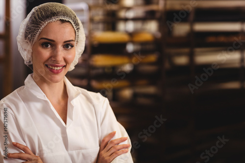 Quadro em tela Smiling woman baker standing inside bakery with hairnet and racks of trays, copy