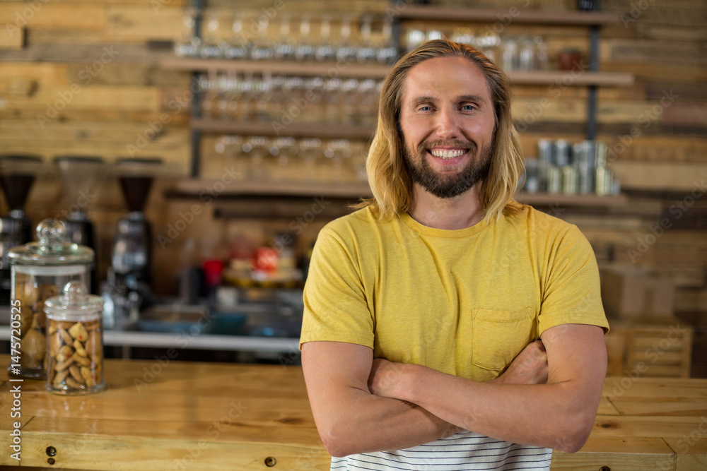 Fototapeta premium Smiling male barista standing behind coffee shop counter, with glass jars and espresso machine