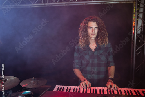 Red keyboard is resting beside drum cymbals on dark stage, illuminated by colored spotlights