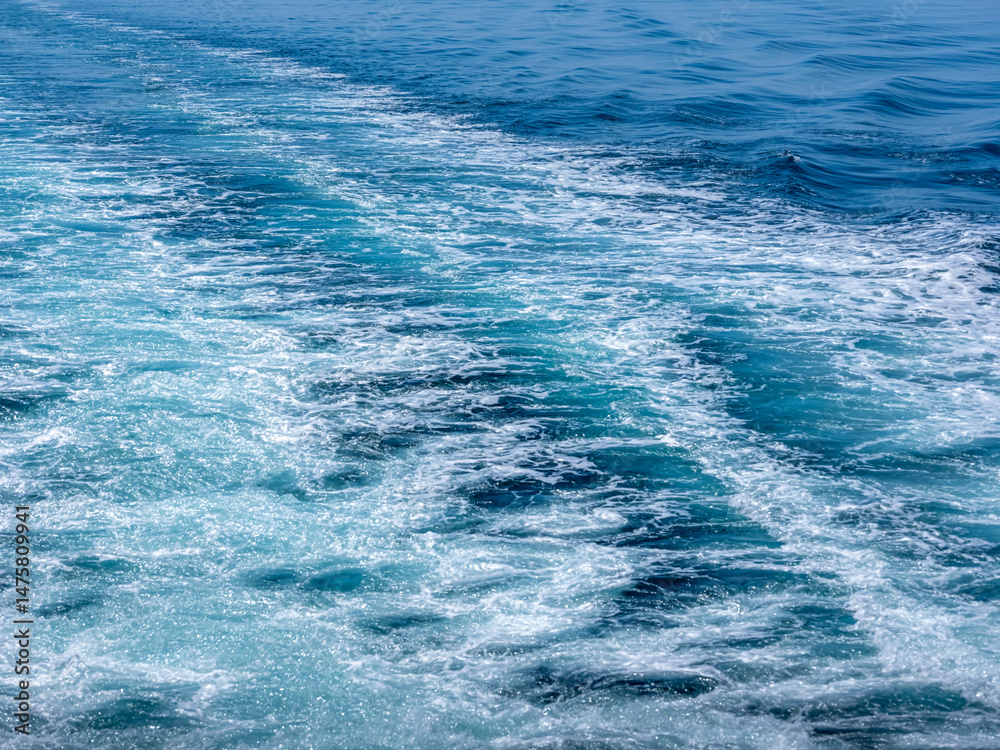 Fototapeta premium 快晴の空と穏やかな海の海上、船舶のスクリューの泡の跡、白とブルーのグラデーションと細かい泡のラインが綺麗です。船跡は右側から左側奥に斜めに流れるラインで横構図です。