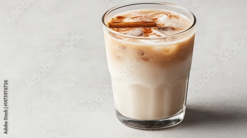 Creamy iced beverage with cinnamon and ice cubes in a transparent glass on a light surface