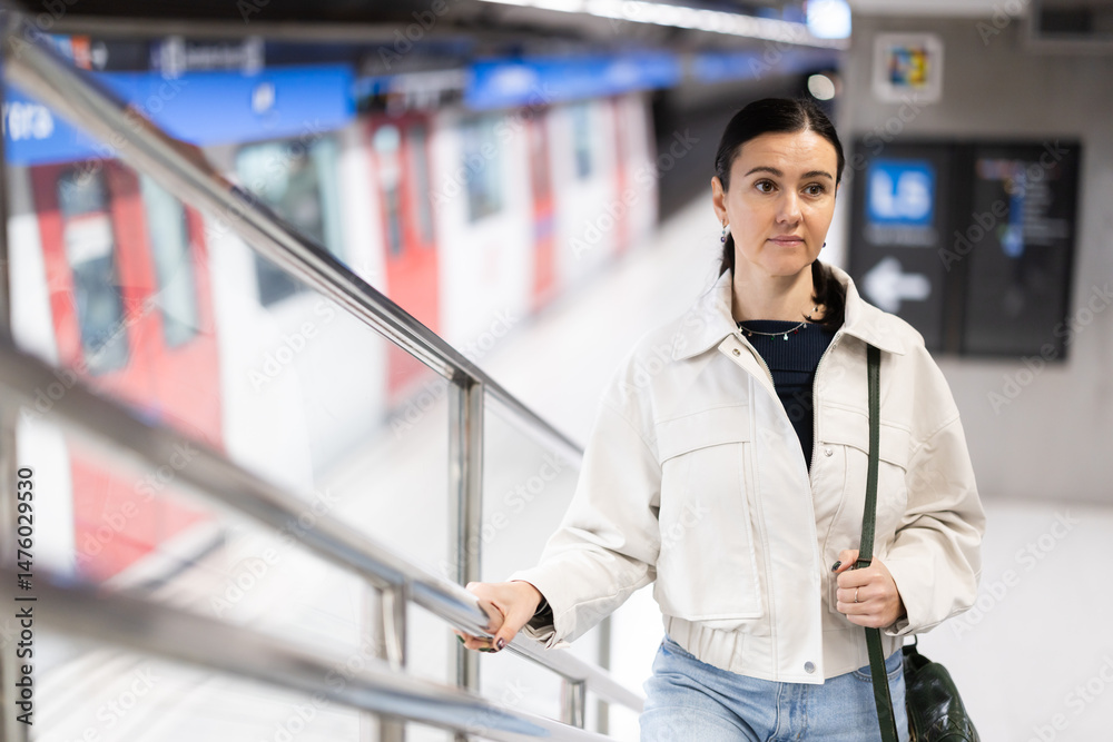 Naklejka premium Woman metro passenger climbs stairs, enters underground public transport station, moves on escalator, stands on moving steps.