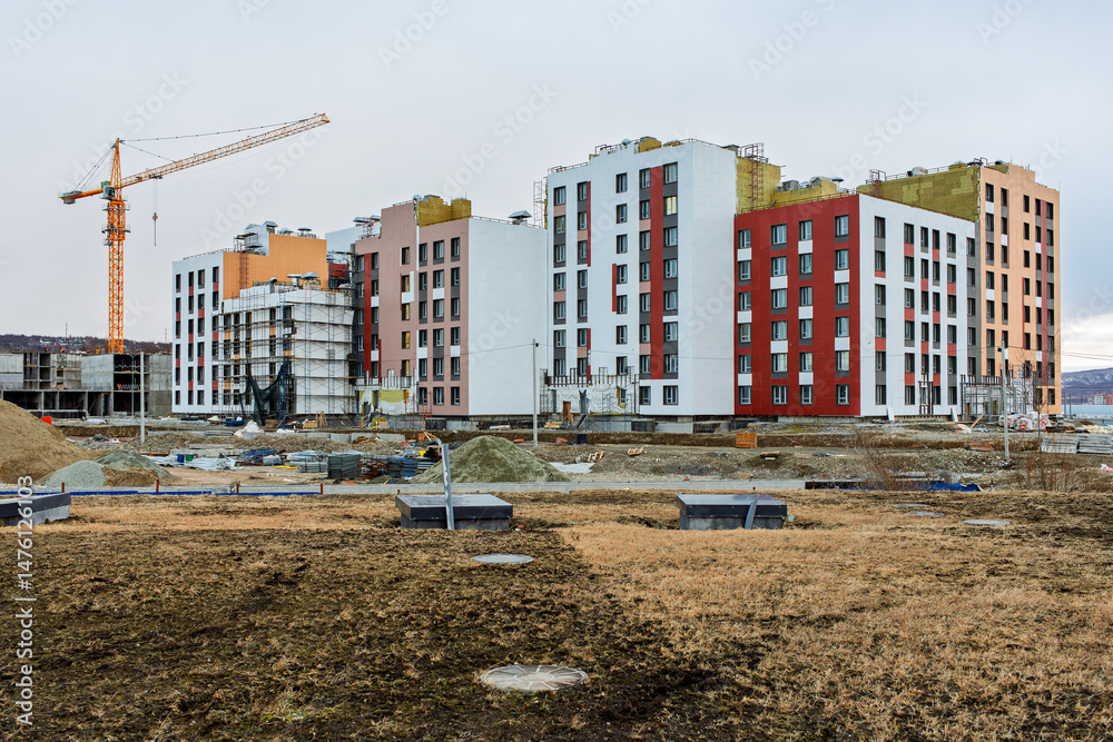 Fototapeta premium Construction of a residential complex. View of the construction site. Construction of a modern multi-apartment residential building. New unfinished building with apartments. Tower crane near the house