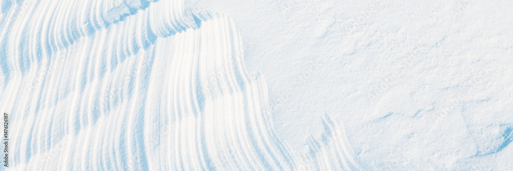 Obraz premium Wide panoramic winter background with snowy ground. Natural snow texture. Wind sculpted patterns on snow surface.