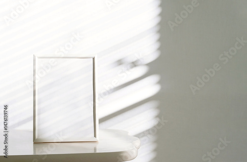 White Picture Frame Rests on Table, Natural Sunlight that Casts Gentle Shadows Through Window Blinds.