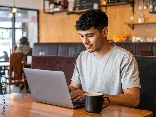 Person Working on Laptop in Cozy Coffee Shop – Half-Empty Mug and Warm Ambience