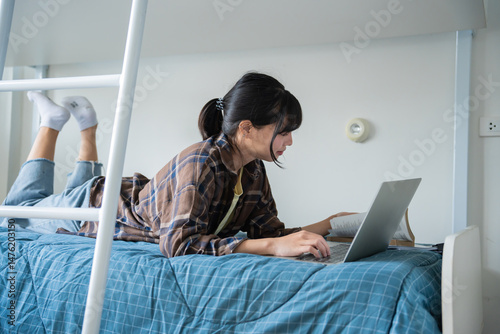 Tableau sur toile Student asian woman lying use laptop on bed in dorm room college student do homework on laptop in university dormitory