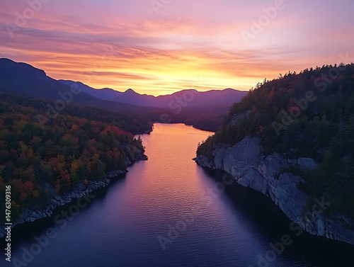Adirondack Mountains with colorful fall foliage and a tranquil lake in view The sky is painted with hues of orange pink and purple as the sun sets behind the mountains casting long shadows