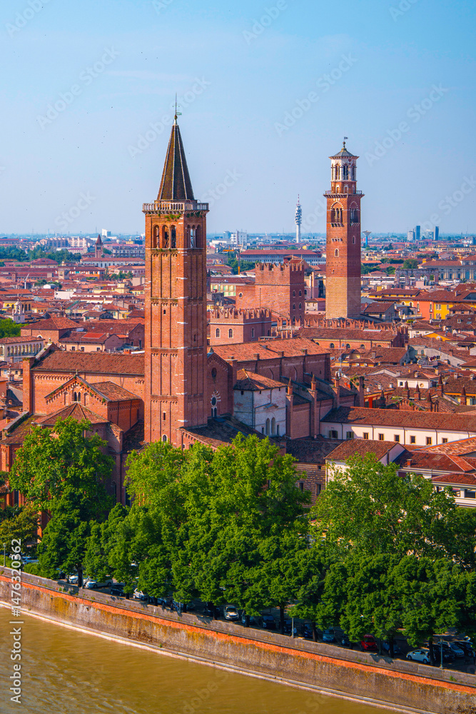 Obraz premium Verona city skyline, church towers, traditional houses, and bridges tracing the curving Adige River in Veneto, Italy—a tranquil metropolitan landscape seen from Piazzale Castel San Pietro hilltop.