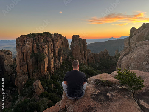 Scenic sunset at the Valley of Desolation with silhouette of a man sitting and admiring the view. A breathtaking moment as the sun sets behind dramatic rock formations and rugged cliffs, casting warm 