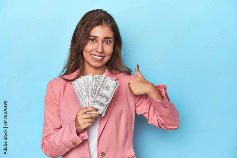 Teen girl in pink, flaunting a handful of dollar bills smiling and raising thumb up Teen girl in pink, flaunting a handful of dollar bills smiling and raising thumb up