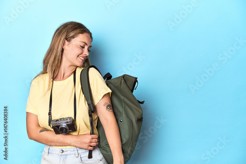 Young blonde traveler with backpack and camera ready for an adventure in a studio