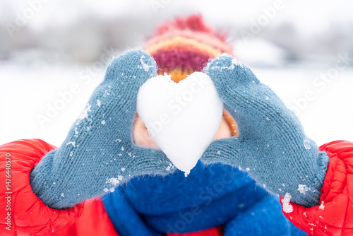 Canvas Print Snowy day joy as child shapes heart from snow in winter landscape wearing colorf