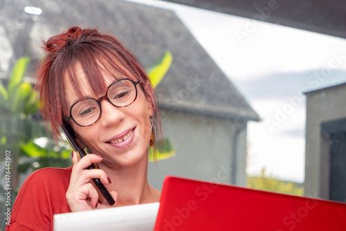 Woman is talking on her cell phone while looking at a red laptop