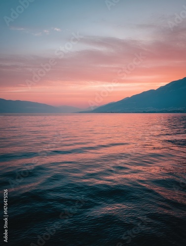 Serene lake at sunset with mountains in background; dreamy pink and blue sky reflecting on water surface; landscape view; tranquil scene