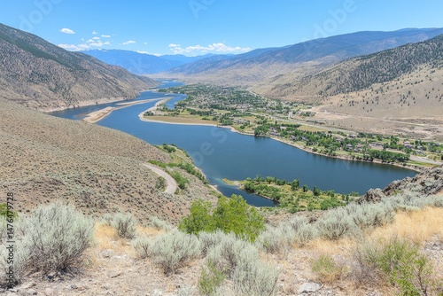 High-altitude view of a winding river valley, a town nestled beside a placid reservoir, and surrounding mountains