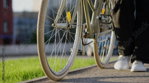 Young fashionable cyclist walking beside bicycle on urban sidewalk, enjoying leisurely movement through modern cityscape with relaxed, carefree stride during sunny daytime