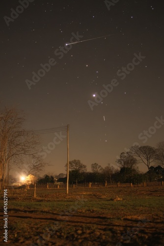Night sky view of shooting star over rural landscape with power pole and trees in foreground