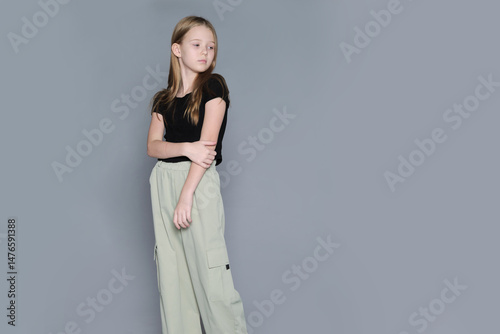 A young girl stands quietly, looking away thoughtfully in a minimalist studio setting. Such emotional portraits address issues of childhood loneliness and the importance of emotional support.
