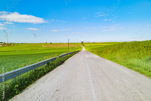 Castellaneta, Italy. Rural road in Puglia, Strada Provinciale 22 from Gioia del Colle to Matera. Surrounded by green fields,  wind turbines, clear blue sky. Clean energy and peaceful countryside.