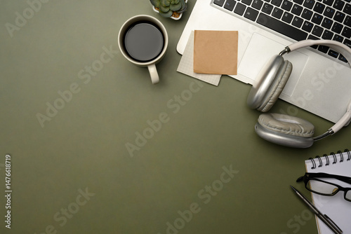 Flat lay of stylish desktop with laptop, coffee cup, headphones, and planner on green desk