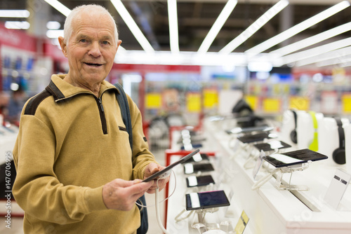 Senor man pensioner buying modern tablet digital in showroom of digital electronic goods store