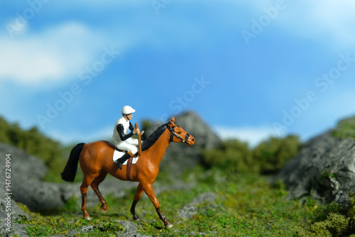 Miniature people toy figure photography. A jockey man riding horse at mountain hill for training