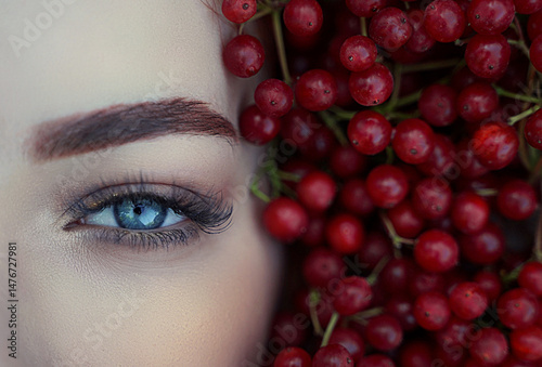 Close-up of a woman's blue eye in red berries.