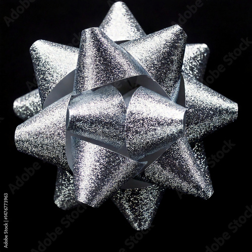 Close up of a sparkling silver gift bow with many pointy petals on a black background, used for decoration and celebration of special events.